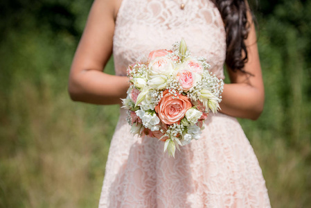 婚礼花束美丽的花朵在新娘的手在白色礼服