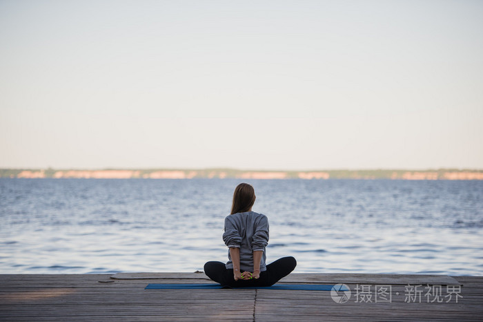 女人在大海或湖泊附近的码头上午做瑜伽的伸展运动