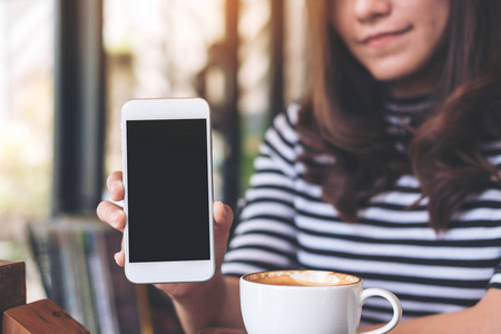 一个美丽的女人手持和显示白色的手机与空白的黑屏和咖啡杯在咖啡馆的图片图像