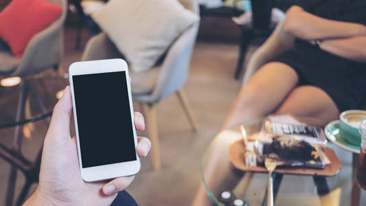 一只手持白色手机, 在现代咖啡馆和背景模糊的亚洲女人手手持白移动电话的样机图像