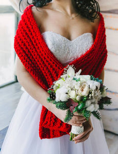 年轻的新娘在一个舒适的大红围巾举行一个漂亮的白色花束看着一边