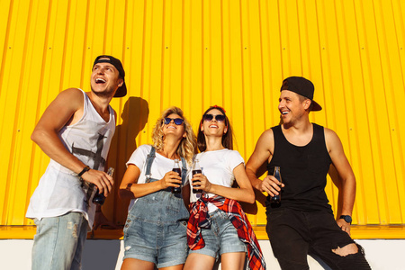 一群年轻人用玻璃瓶喝着饮料站在超市附近, 在黄色的背景下, 朋友们带着饱满欢快的心情, 阳光明媚的日子, Lifestyl 的