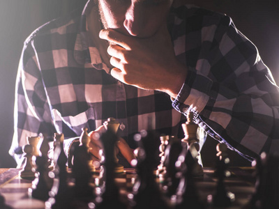 年轻的不被认出的男性人认为在棋板概念附近以黑暗的背景