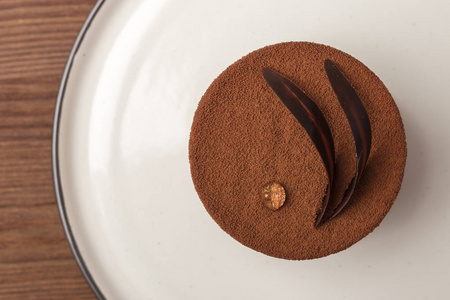 巧克力蛋糕放在盘子上, 用一滴露水和巧克力叶子缠结在一起。手工。木质背景。从上面查看