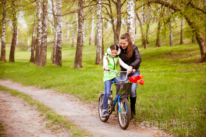 快乐妈妈教他女儿骑一辆自行车.母亲抱着女儿从下降