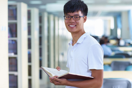 年轻的男大学生看图书馆中的相机微笑