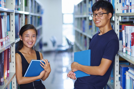 两个年轻的亚洲大学生笑在图书馆里的相机