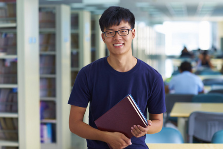 年轻的男大学生看图书馆中的相机微笑照片