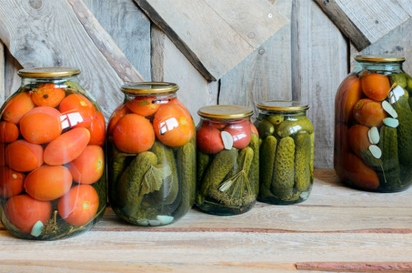 一排玻璃罐, 西红柿和黄瓜罐头。木质背景。乡村风格