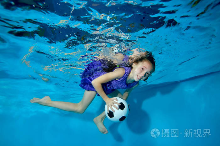 一个带着足球的小女孩在她的手里从事体育运动在泳池里游泳穿着紫色的