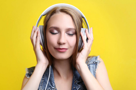 在黄色背景下听音乐的年轻妇女在耳机上