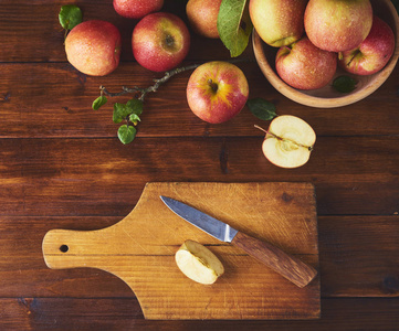 新鲜成熟的苹果在碗里, 切板与刀和一半苹果在木褐色背景