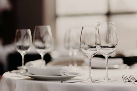 水平镜头的精美服务表与白色桌布, 空酒杯, 叉子, 盘子和餐巾对模糊的背景在豪华餐厅