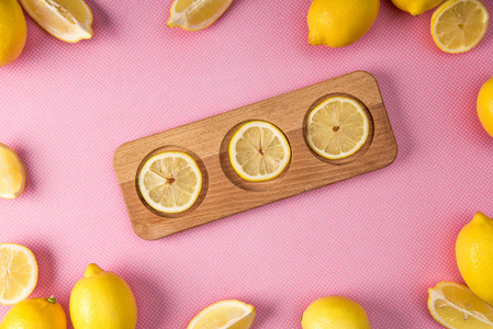 在粉红色背景下柠檬木板上新鲜柠檬片的顶部视图