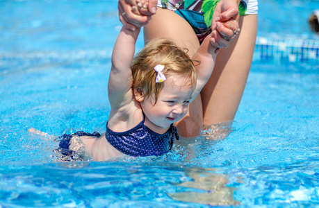 宝贝女孩要学会在与她的母亲的游泳池里游泳