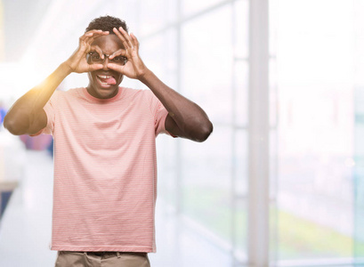 年轻的非洲裔美国人穿粉红色 t恤做 ok 手势像望远镜伸出舌头, 眼睛看通过手指。疯狂的表情