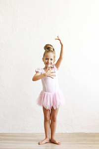 小金发 balerina 女孩跳舞和摆在舞蹈俱乐部与木 floot 白色质感石膏墙。年轻的芭蕾舞演员穿着粉红色的短裙, 有乐趣和