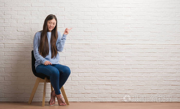 坐在椅子上的年轻的中国妇女用手和手指在墙壁非常愉快指向边