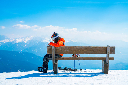 Saalbach, 奥地利。2018年3月20日。年轻的滑雪男子坐在山顶上的阿尔卑斯山看着地平线。欣赏滑雪胜地。滑雪