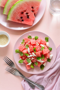 夏季西瓜沙拉配有羊乳酪, 芝麻籽和薄荷叶放在粉红色的盘子里。健康饮食理念