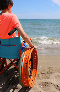 小男孩在特别轮椅与大轮子在海滩的沙子容易地移动