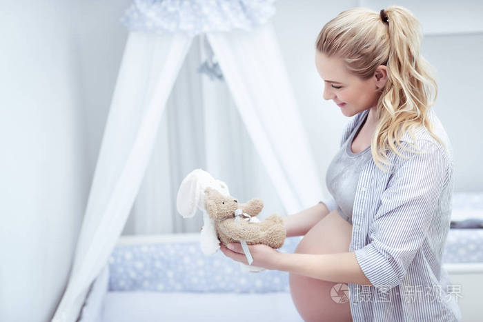 快乐的母亲准备孩子的房间, 美丽的年轻孕妇与乐趣装饰床她未来的婴儿