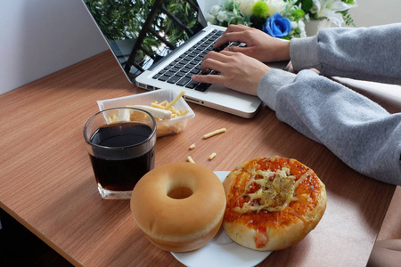 在使用笔记本电脑时, 用甜甜圈面包比萨饼和可乐水饮料吃零食