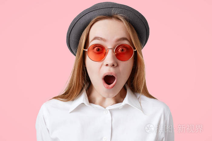 坦率的拍摄惊讶的吓坏了女性与宽大张开的嘴, 身着白色衬衫, 黑色时尚