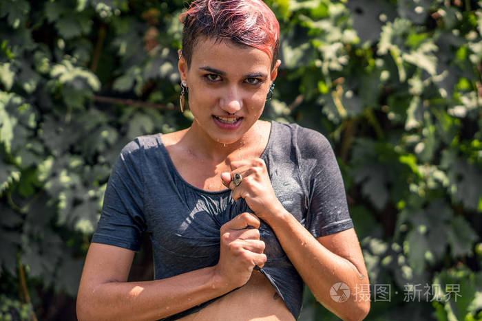 年轻漂亮的穿湿衬衫的女孩, 淋浴后, 从软管在花园.