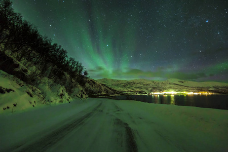 北极极光在黑夜中熄灭。一个北极, 下雪的冬季景观与道路和峡湾的前景。天空是清澈的, 星星是可见的