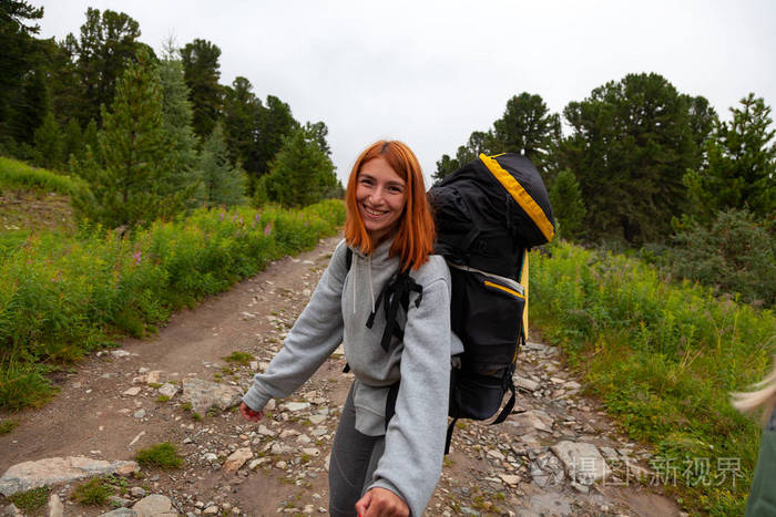 徒步旅行的妇女带着背包乐呵呵地微笑着, 在山上远足。时髦的游客在森林的顶端, 令人惊叹的景色。流浪乐趣和旅行 concep