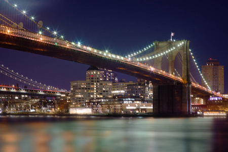 曼哈顿大桥和布鲁克林天际线在河里的美丽模糊的反射在夜间