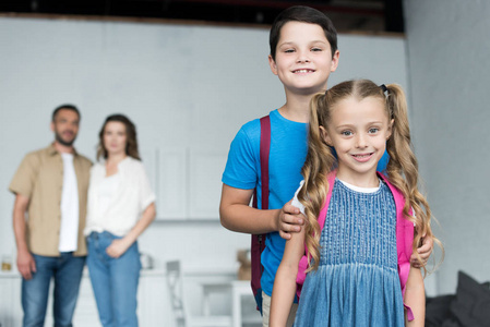 有选择的焦点微笑的兄弟姐妹与背包和父母后面, 回到学校概念