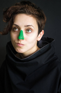 图片照片肖像的女孩卷曲短发和绿色油漆在她的鼻子黑色的衣服与高领鬼脸暗背景