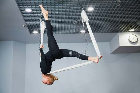 美丽的健身模型在飞行瑜伽吊床。杂技女子运动反重力空中瑜伽练习