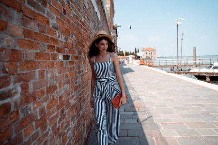 一个年轻的女孩沿着威尼斯的海滨散步。她手里握着一把离合器。天气晴朗