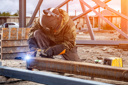 棕色通道一个年轻男子焊工在棕色制服, 焊接面具和焊工皮革, 焊接金属