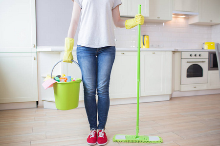 妇女立场的切开的看法在厨房和举行棍子与拖把在一只手和桶与清洁设备在另一。女孩戴黄色手套