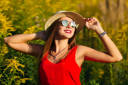 一个女孩在时尚的帽子和太阳镜可爱的笑容和站在高草