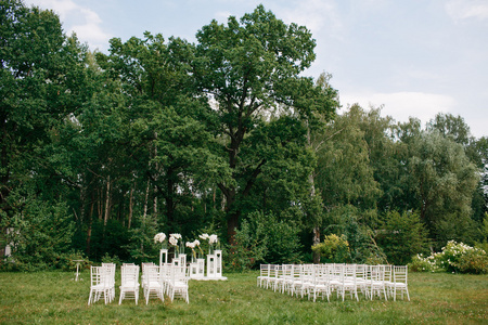 婚礼在一个美丽的花园。白色的桌椅镜像。玻璃花瓶与花马蹄莲百合朱顶兰
