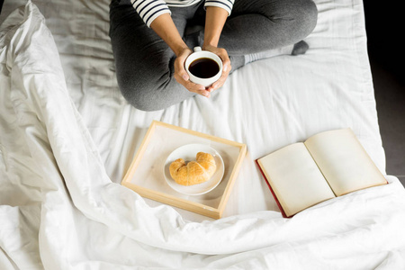 妇女读书或报纸和喝咖啡早餐在床上在早晨
