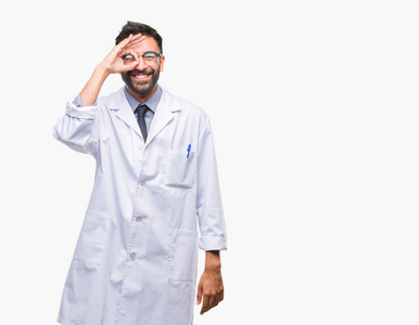 成人西班牙裔科学家或医生穿白色大衣在孤立的背景下做 ok 手势用手微笑, 眼睛看通过手指与愉快的面孔
