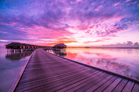 在马尔代夫的日落, 豪华的水上别墅度假村和木码头。美丽的天空和云彩和海滩背景为暑假假期和旅行概念
