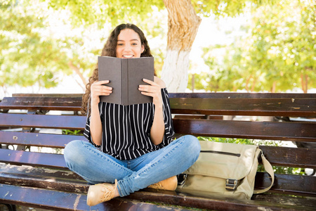 年轻的西班牙裔女孩的肖像喜欢读一本公园长椅上的书