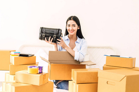 年轻妇女自由职业者工作中小型企业在线购物和包装妇女袋在床上的纸板盒在家里企业在线送货和送货概念