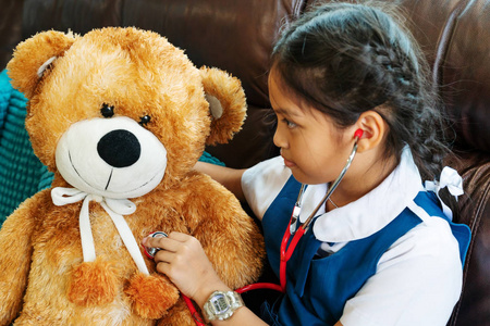 小女孩笑着, 打着棕色熊和听诊器的医生。儿童与医疗保健概念