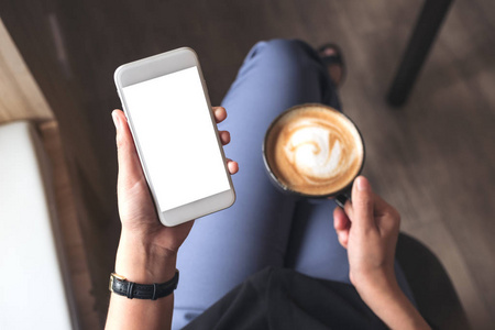 在咖啡馆里喝咖啡时, 一个女人手捧着白色手机, 手持空白桌面屏幕的图片