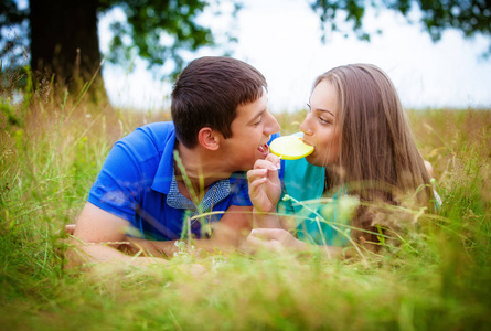 浪漫的年轻夫妇与糖果躺在绿色的草地上公园
