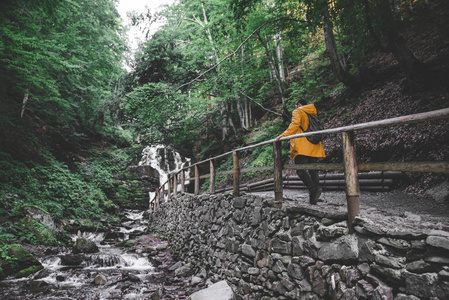 男子走在森林小径到瀑布的黄色雨衣。旅游理念