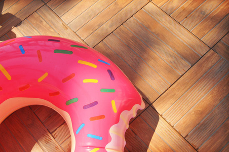 棕色木地板上的大充气粉红色甜甜圈游泳戒指